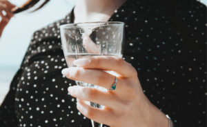 A person wearing a black shirt with small, white polka dots, holding a wine glass half full of water.