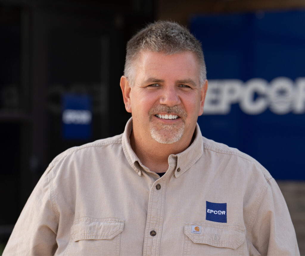 A portrait of a man with short salt and pepper hair wearing a tan shirt with the Epcor logo above the left pocket.