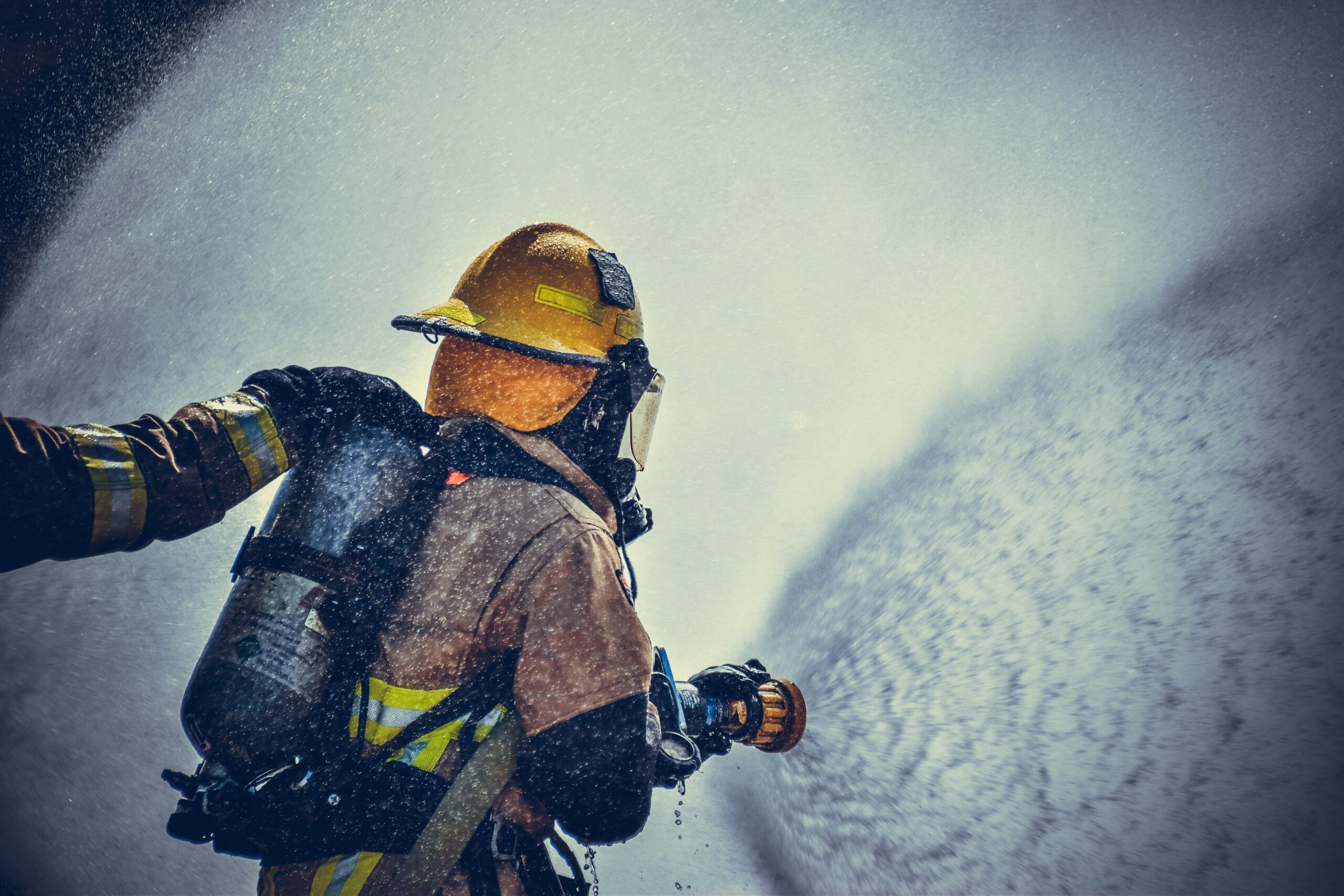 A firefighter holding a firehose at full blast.