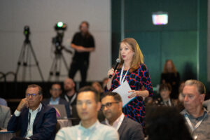 A woman from the audience standing asking a question into the microphone for panelists to discuss