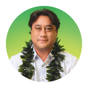 Photo of John “Kani” Kadowaki, green background, white shirt and wearing a lei